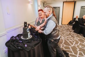 Couple cutting a gothic-themed black wedding cake using an axe-shaped cake-topper knife