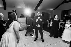 Black and white reception dance floor with the groom dancing under stage lights and 'Happily Ever After' sign behind