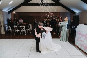 Groom dipping the bride for a kiss during their first dance, confetti falling around them
