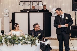 Best man giving a speech beside the seated bride and groom at the top table