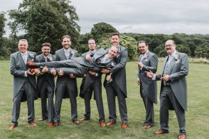 Groomsmen lifting the groom horizontally for a playful group photo on a lawn