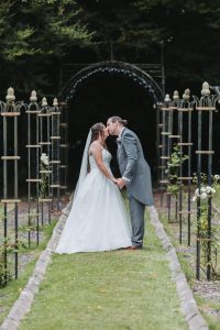 Bride and groom kissing in a garden archway lined with iron trellis posts