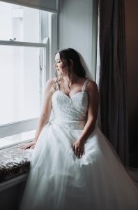 Bride seated on a window seat in dramatic side light, gazing out of the window