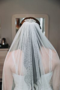 Bride from behind showing her veil and decorative hair comb in front of a mirror