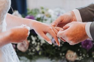 Ring exchange during the ceremony — groom placing the ring on the bride's finger over a floral altar