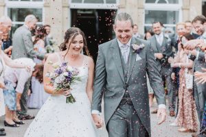 Bride and groom walking through a confetti shower outside the ceremony venue