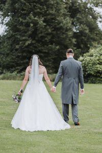 Bride and groom walking hand in hand on a lawn, viewed from behind