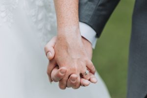Close-up of a bride and groom holding hands, wedding and engagement rings visible